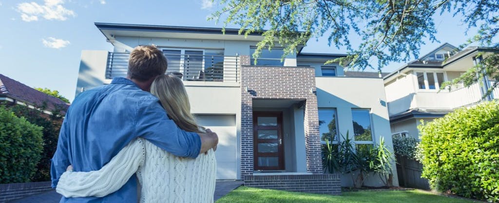 Young couple, seen from behind, arms around each other, looking at their new home and wondering what they should know about tax reform for homeowners.