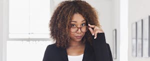 Young African-American woman peering over her glasses, skeptical of common tax refund myths.