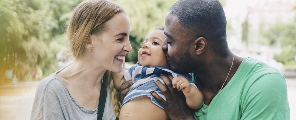 Smiling interracial couple holding their baby.