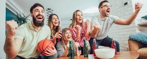 A group of young adults watching a basketball game together in a home, and cheering for their team.