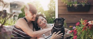 Female couple at home, sitting on their patio, with their dog, a small black pug