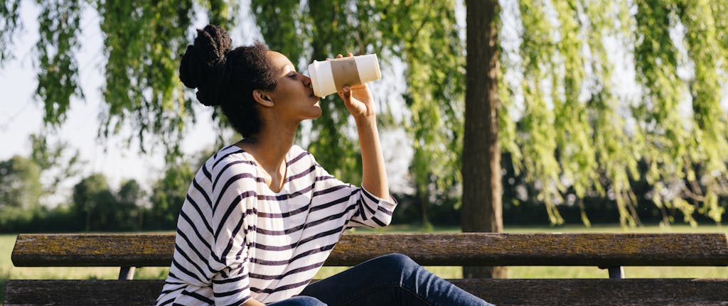 Young woman sitting on park bench drinking coffee to go