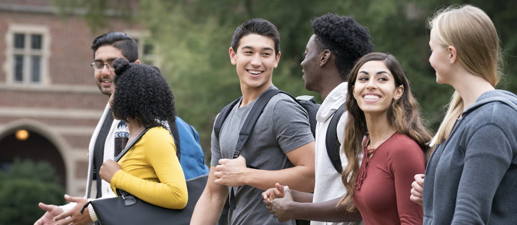Group of young diverse college students smiling, talking and walking across campus