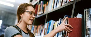 Happy young woman removing a book from a shelf in a college library
