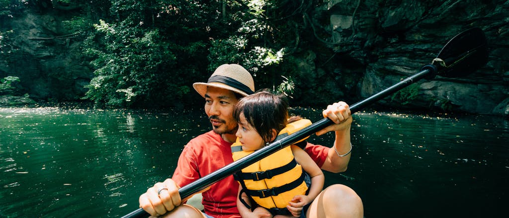 Father and his little girl paddling a packraft together on a river in a tropical environment