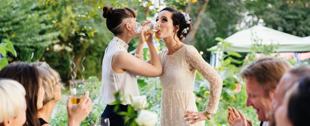Brides link arms to drink champagne in celebration of their marriage.