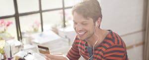 Man smiling while looking at his credit card, headphones in his ears