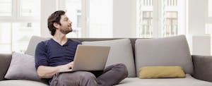 Man sitting on couch using laptop, looking hopeful