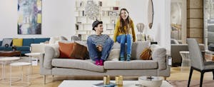 Couple in modern furniture store sitting on couch, laughing and wondering about the difference between their FICO score and credit score.