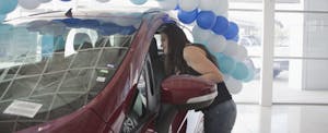 Young Hispanic woman looking at a car in a dealer showroom.
