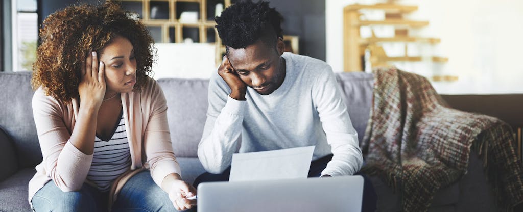 A young high-earning couple anxiously discusses their finances on the couch. They weren't expecting so many unexpected expenses and emergency costs to come up in one year and they need to borrow money to pay for it all.