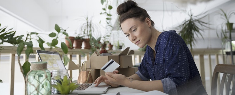 Female plant shop owner with credit card paying bills online at laptop in workshop