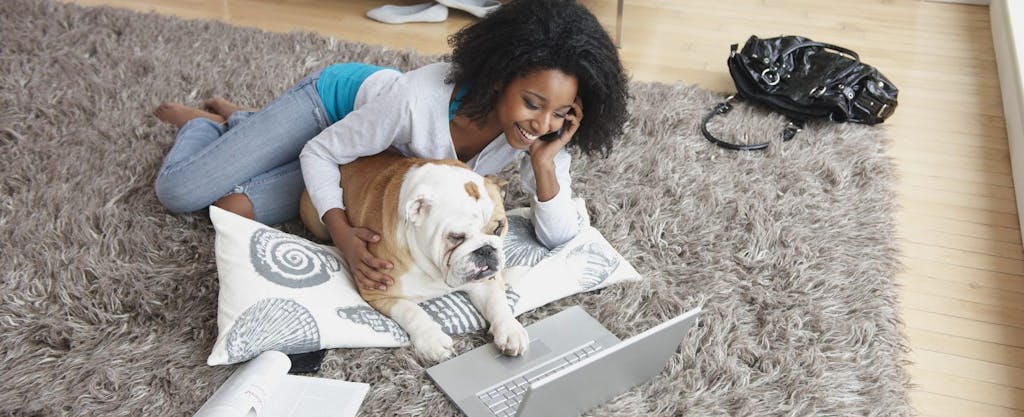 Young African-American woman laying on rug with dog and her laptop, determining what tax deductions and credits she can carry forward.