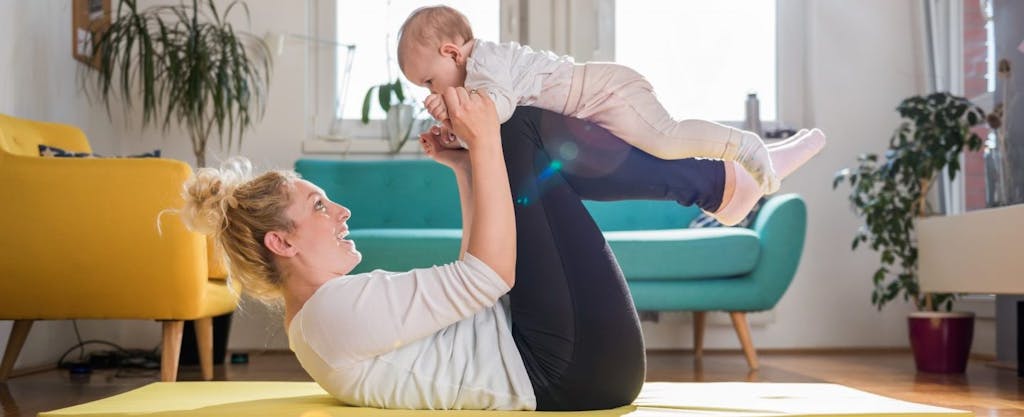 Mother exercising at home doing floor yoga with her baby.