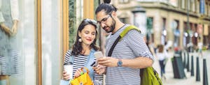 Man and woman look at mobile phone while shopping on city street.