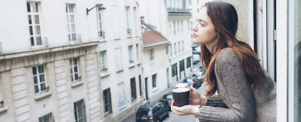 Young American woman living abroad, sipping her morning coffee while looking out the window and wondering how the foreign earned income exclusion could affect her federal income taxes.