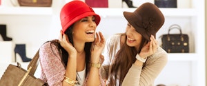 Two young women try on hats while shopping.