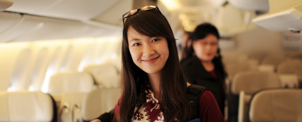 A smiling woman stands in the aisle of a passenger aircraft.