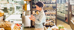 Young woman with headphones using cell phone, grocery shopping in market