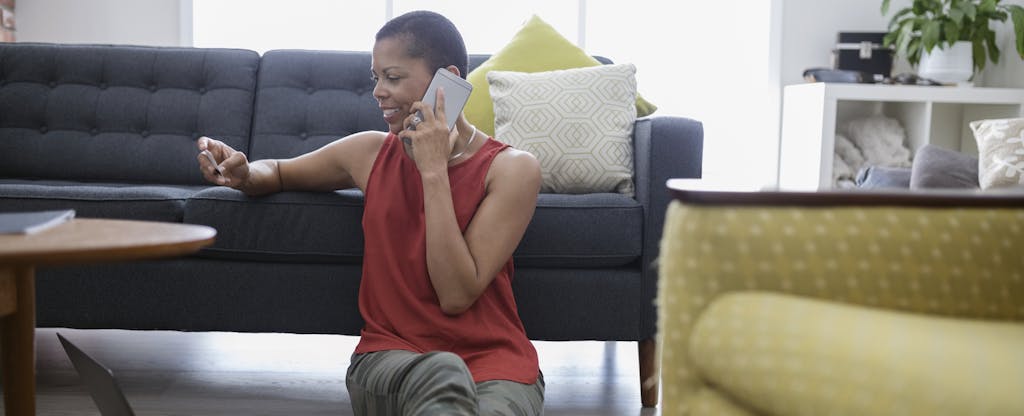 Mature woman with credit card talking on cell phone, using credit card at laptop on living room sofa