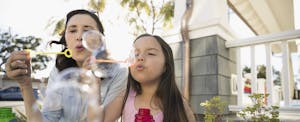 Grandmother and granddaughter blowing bubbles on summer porch