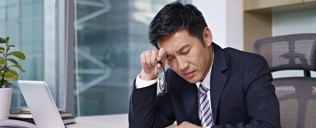 Asian businessman contemplating Form 14039, sitting in office and looking tired.