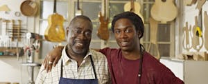 Craftsman in his guitar workshop with son