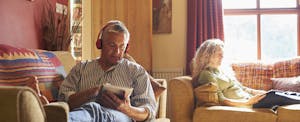 Older couple sitting on sofas using digital tablets
