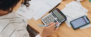 Top view of a woman working at home in the kitchen with financial papers, counting on a calculator, paying bills, planning a budget to save some money.