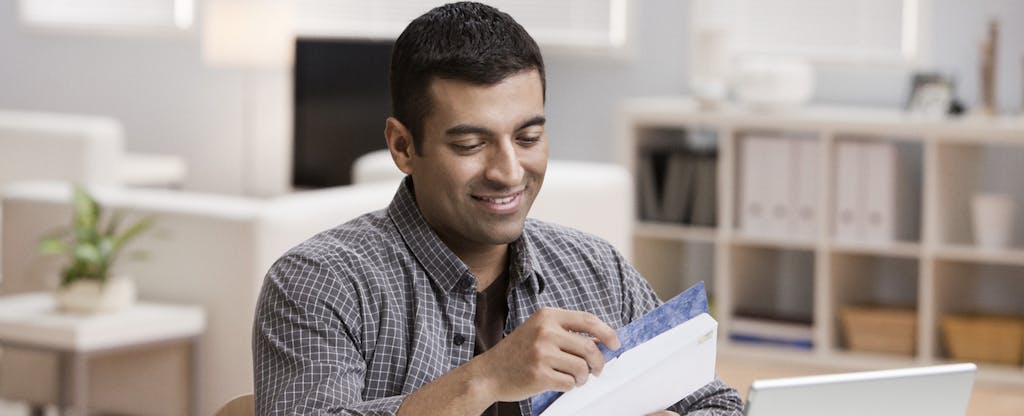A man opens mail in his home office, hoping to hear back about a small personal loan.