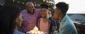 African American family celebrating graduation with cake on summer deck, worried about how student loan debt might affect their graduate's life in the future.