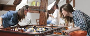 Two young female office workers happily enjoying a fringe benefit of their workplace: a foosball table.