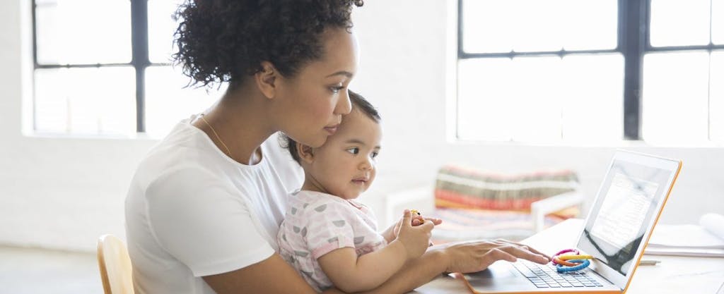 African-American mother holding baby on her lap while researching the child tax credit on her laptop.