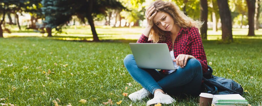 A young woman, sitting outside in the grass, looking at her laptop and wondering how to calculate AGI