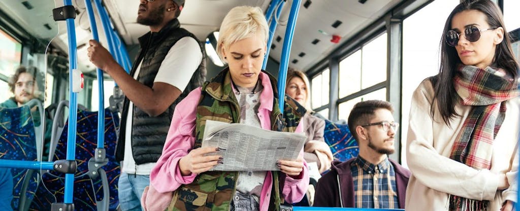 Young woman reading the classifieds on the bus, unaware that if she gets unemployment payments she will also get a 1099-G form at tax time.