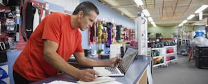 Business owner working at laptop at counter in home gym equipment store