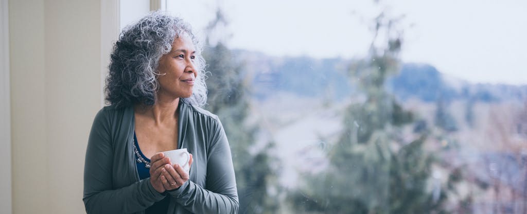 Mature woman looking pensively out her window.