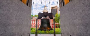 The Liberty Bell, a Pennsylvania landmark, in close up with Philadelphia's city hall in the distance behind it.
