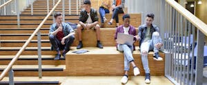Multi-racial group of college students sitting on stairs and discussing college tax credits that could help them or their parents reduce their federal income tax burden.