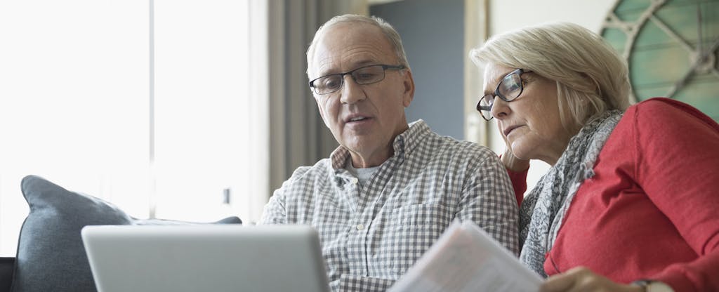 Senior couple looking at paperwork and using laptop