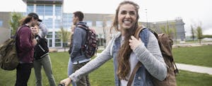 Smiling female college student with backpack on lawn on college campus