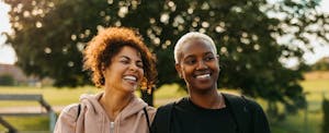 Two friends sitting and smiling together in the park after finishing a workout