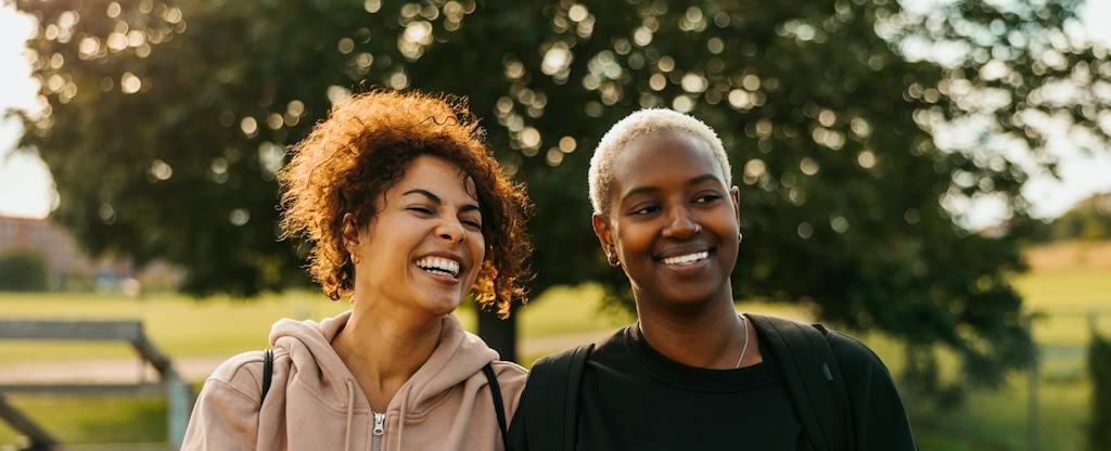 what-is-a-checking-account Two friends sitting and smiling together in the park after finishing a workout