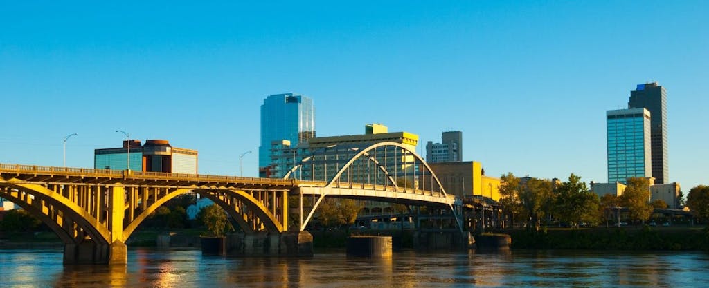 Downtown Little Rock, the capital of Arkansas, is seen in the background with the scenic arch of the Pike Avenue Bridge spanning the Arkansas River in the foreground.