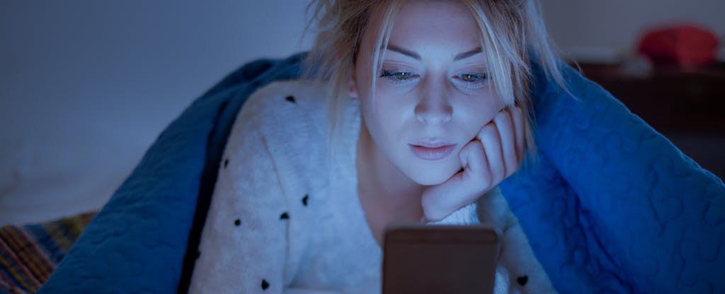 Woman holding mobile phone and online holiday shopping while laying on bed at night