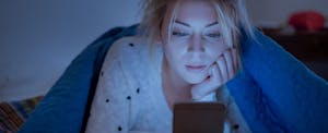 Woman holding mobile phone and online holiday shopping while laying on bed at night
