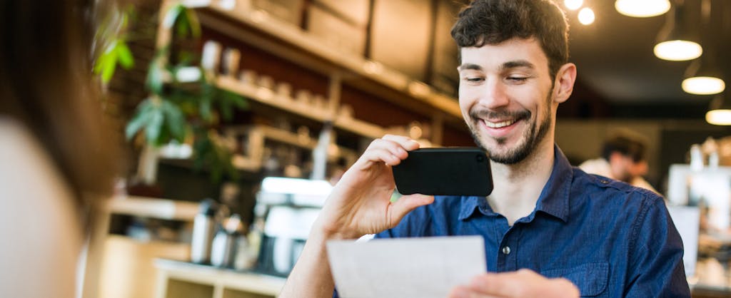 A smiling man takes a picture with his smart phone of a check or paycheck for digital electronic depositing.
