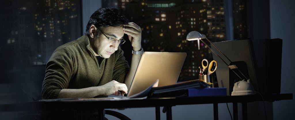 Businessman working late in office, looking worried as he checks his laptop