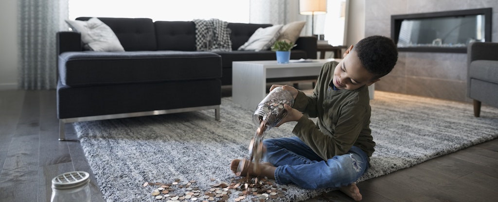 Boy emptying coins from jar onto living room floor