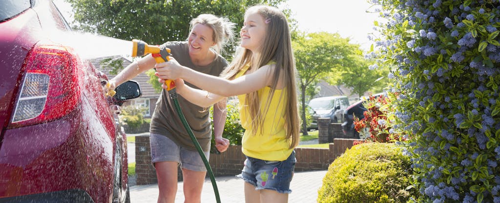 Mother and daughter washing car in sunny driveway